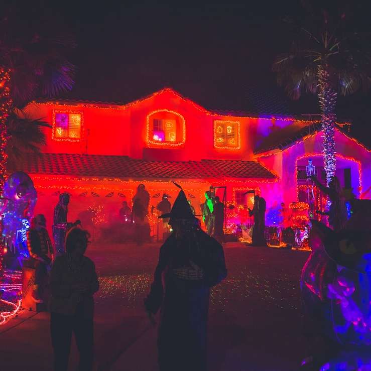 människor som står nära hus med rött ljus dekor Pussel online