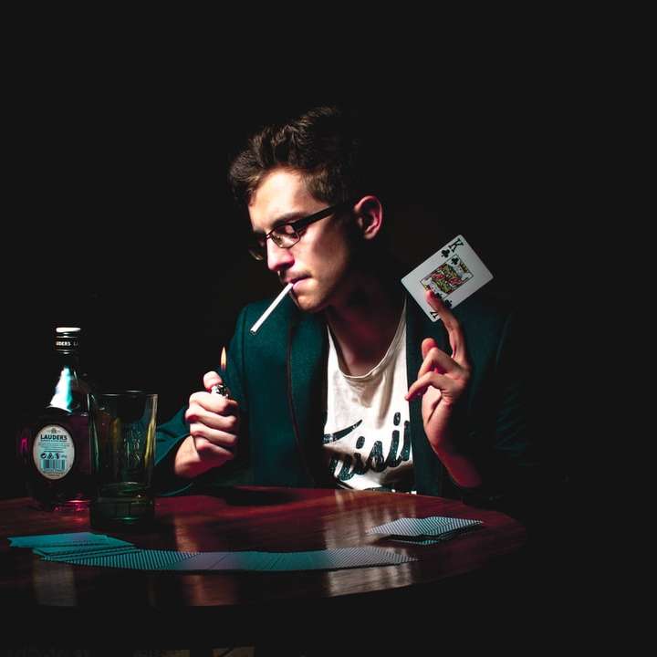 man lighting cigarette while holding playing card online puzzle